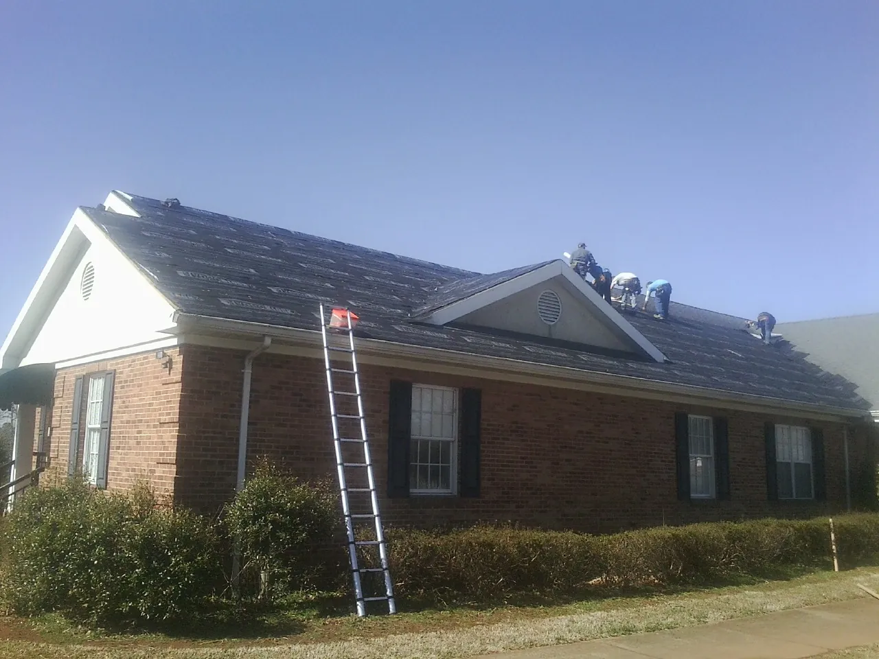 Crew tearing shingles off a brick ranch roof with a ladder set — Emergency Roof Repair work by our crew in Branch