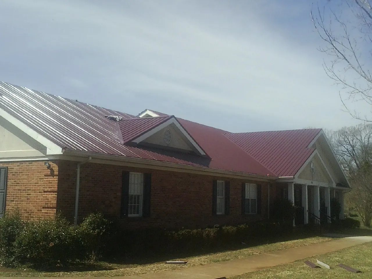 Red metal roof with gabled entries on a long brick building, from a Hail Damage Roof Repair job in Branch